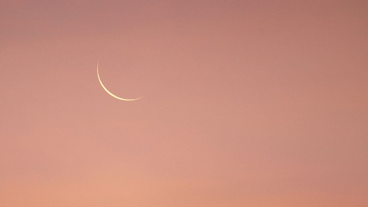 Schmale Mondsichel vor orange gefärbtem Himmel
