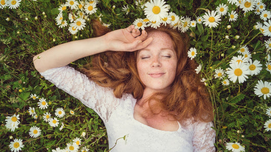 Rothaarige Frau liegt lächelnd in Blumenwiese